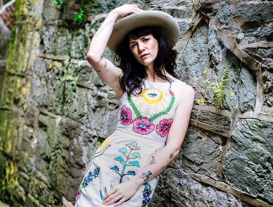 A woman in a wide-brim hat wearing a cream Fort Lonesome dress with colorful chainstitch floral embroidery