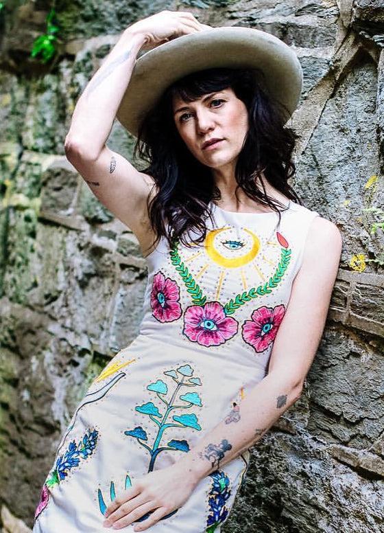 A woman in a wide-brim hat wearing a cream Fort Lonesome dress with colorful chainstitch floral embroidery