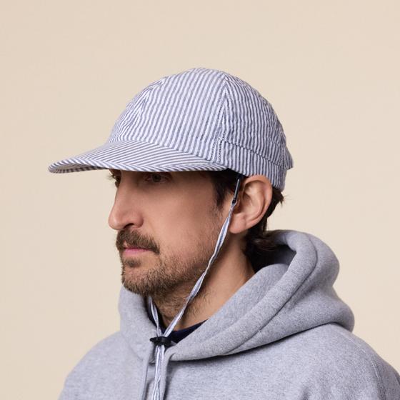 A man wearing a blue and white striped seersucker Found Feather cap with chin cord