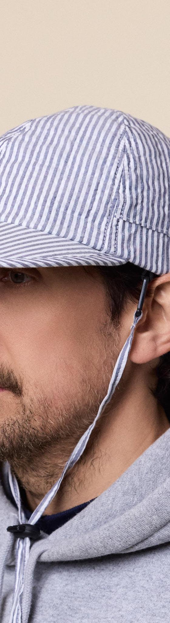A man wearing a blue and white striped seersucker Found Feather cap with chin cord