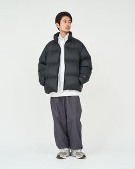 A man wearing a black FreshService puffer down jacket over a white half-zip with grey nylon pants