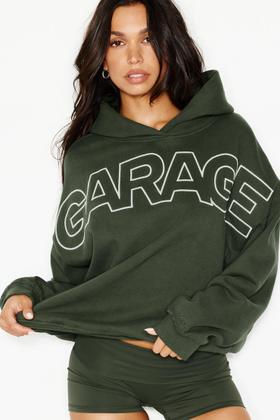 A woman wearing a dark green oversized Garage logo hoodie with matching shorts