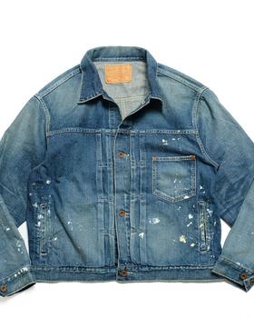 A faded blue denim trucker jacket with paint splatters, laid flat on a white background