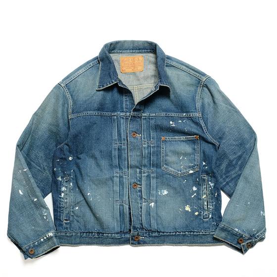 A faded blue denim trucker jacket with paint splatters, laid flat on a white background