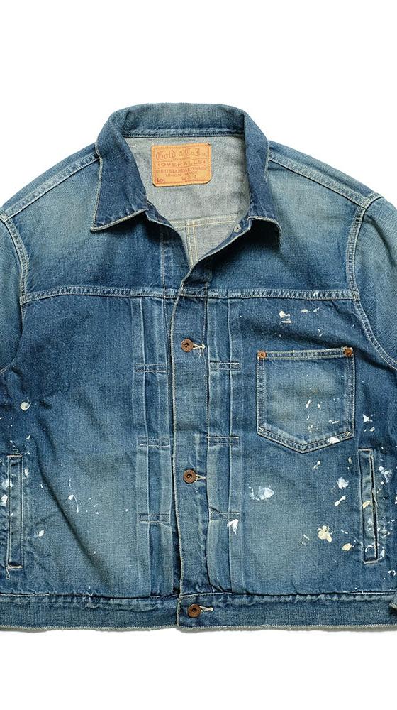 A faded blue denim trucker jacket with paint splatters, laid flat on a white background