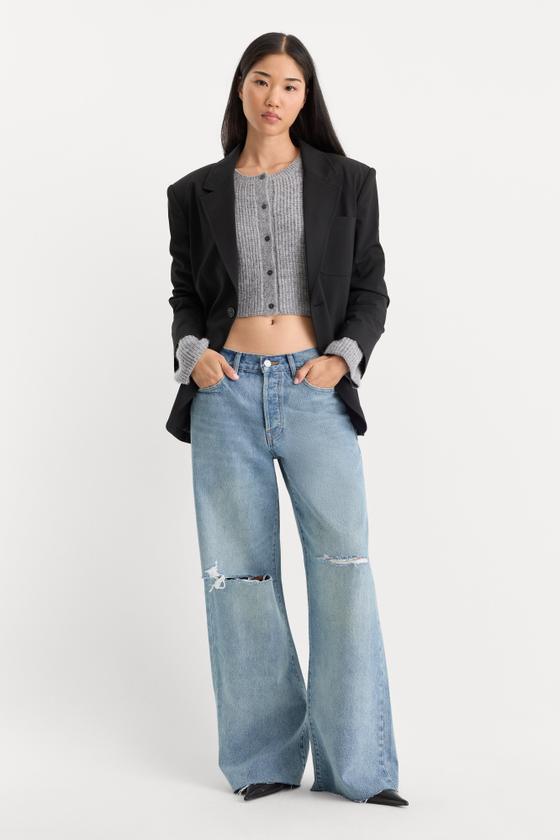 A woman wearing wide-leg distressed Good American jeans with a grey cropped cardigan and black blazer