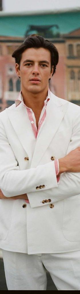 A man wearing a white double-breasted blazer and matching trousers over a pink-striped shirt