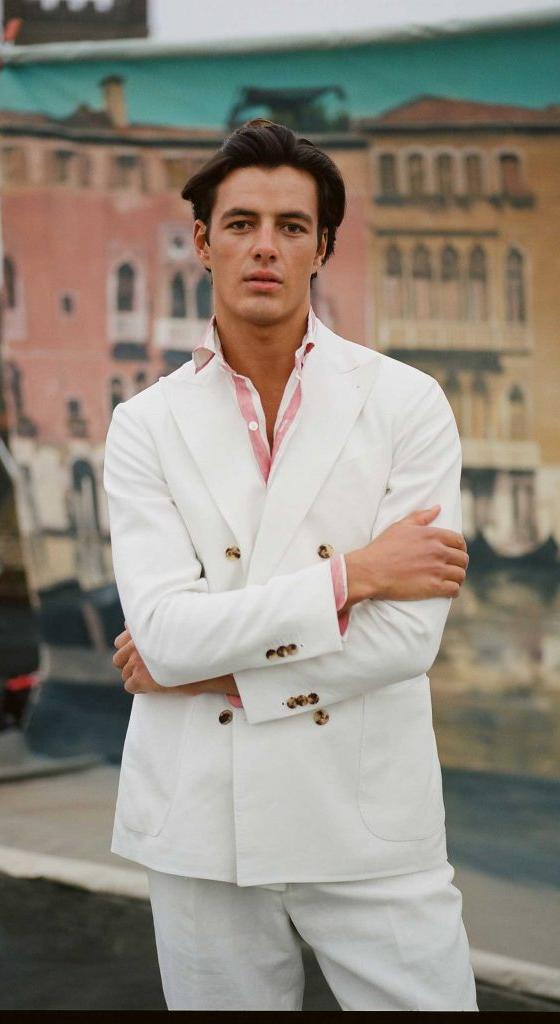 A man wearing a white double-breasted blazer and matching trousers over a pink-striped shirt