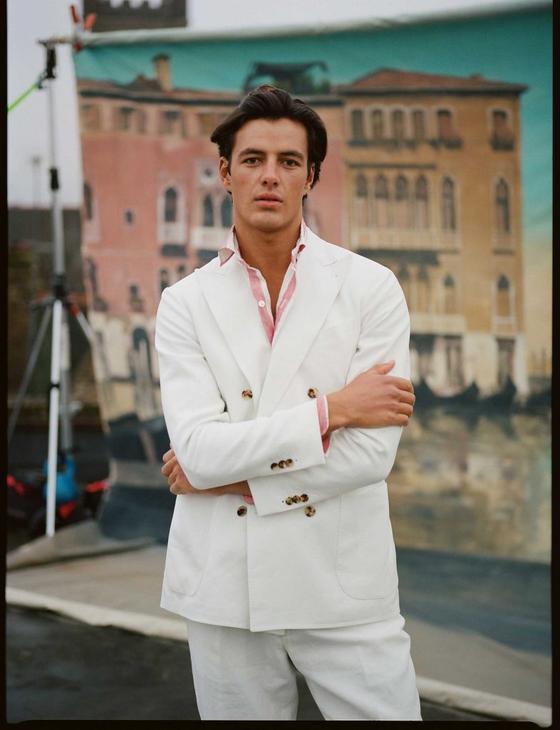 A man wearing a white double-breasted blazer and matching trousers over a pink-striped shirt