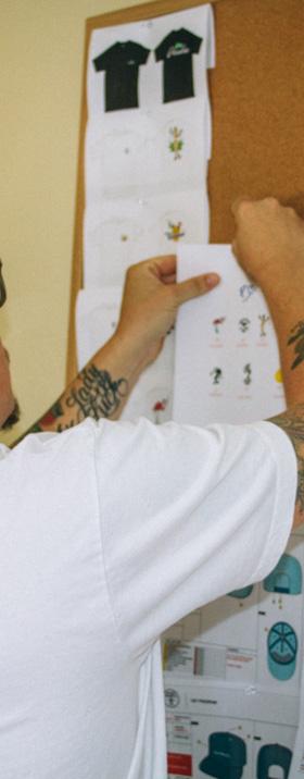A man in a white T-shirt pinning Good Worth & Co. design sketches to a studio corkboard