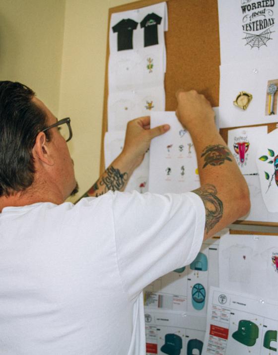 A man in a white T-shirt pinning Good Worth & Co. design sketches to a studio corkboard