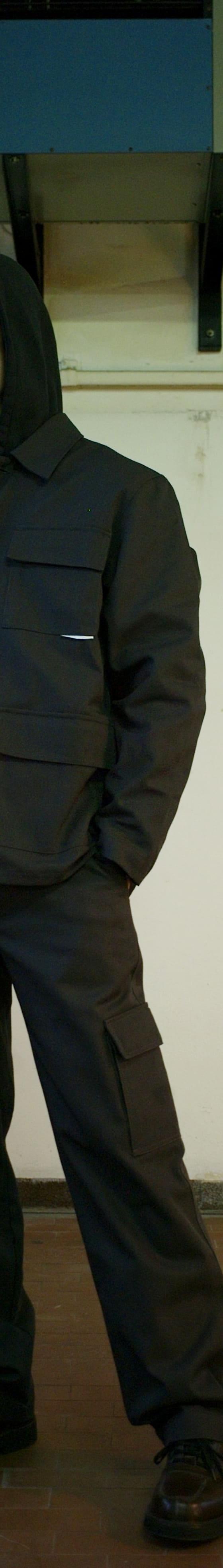 A man wearing a dark hooded GR10K utility jacket with cargo trousers