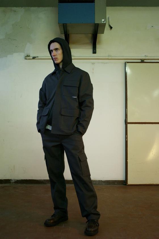 A man wearing a dark hooded GR10K utility jacket with cargo trousers