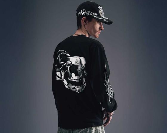 A man wearing a black Greedy Unit long-sleeve tee and printed cap, photographed from behind
