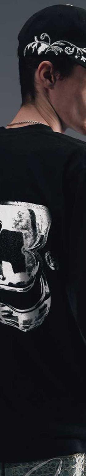 A man wearing a black Greedy Unit long-sleeve tee and printed cap, photographed from behind