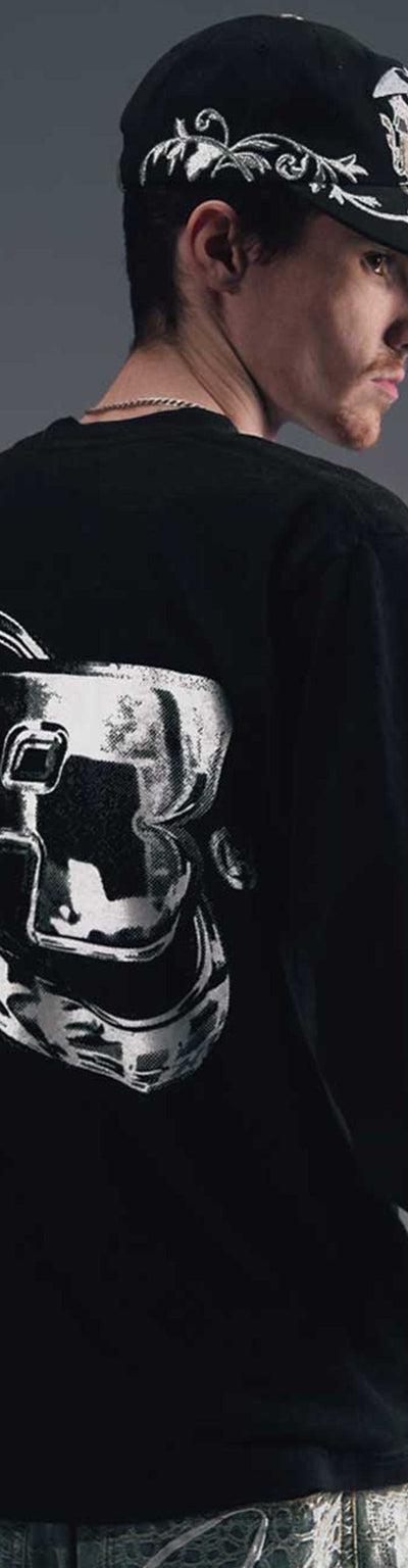 A man wearing a black Greedy Unit long-sleeve tee and printed cap, photographed from behind