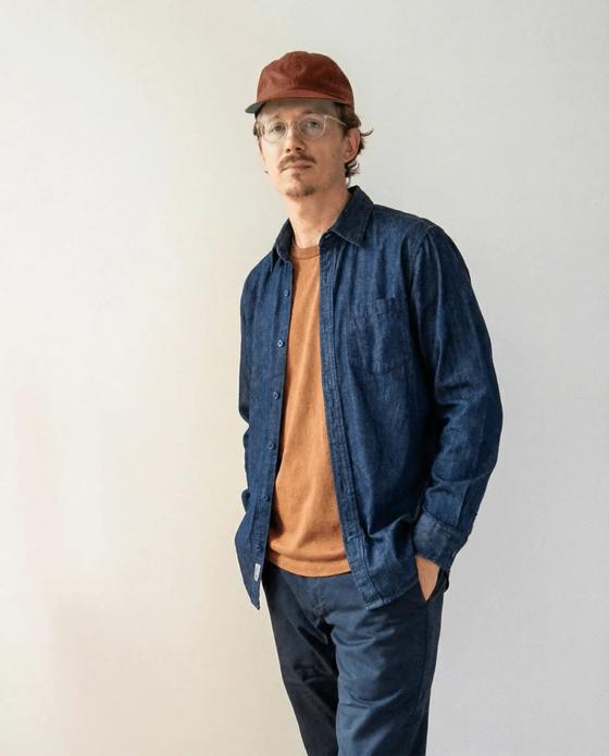 A man wearing an indigo denim work shirt over a rust tee with navy chinos