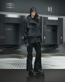 A man wearing a black Guerrilla-Group technical hooded jacket with matching zip-detail trousers