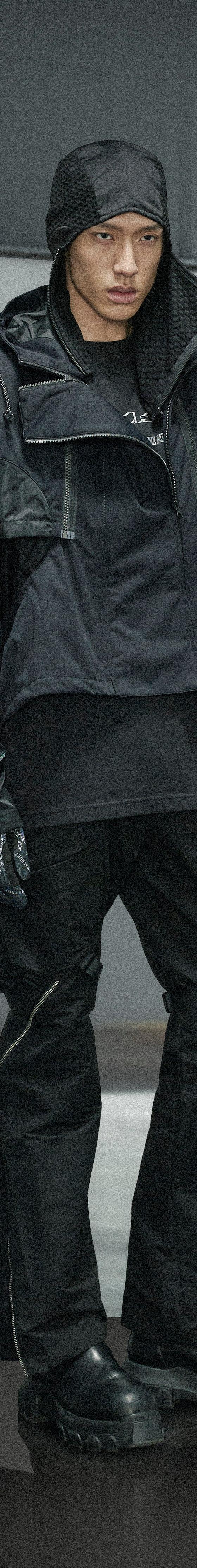 A man wearing a black Guerrilla-Group technical hooded jacket with matching zip-detail trousers