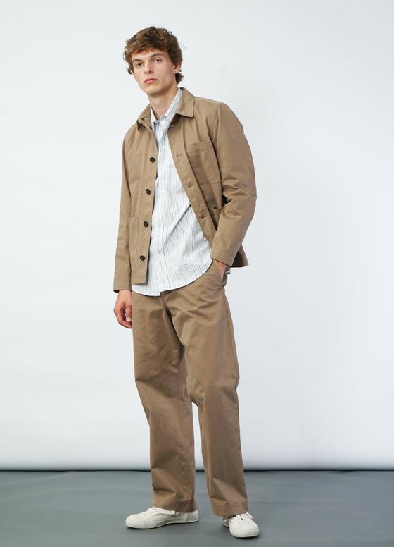 A man wearing a tan Hansen Garments chore jacket over a striped shirt with wide beige trousers