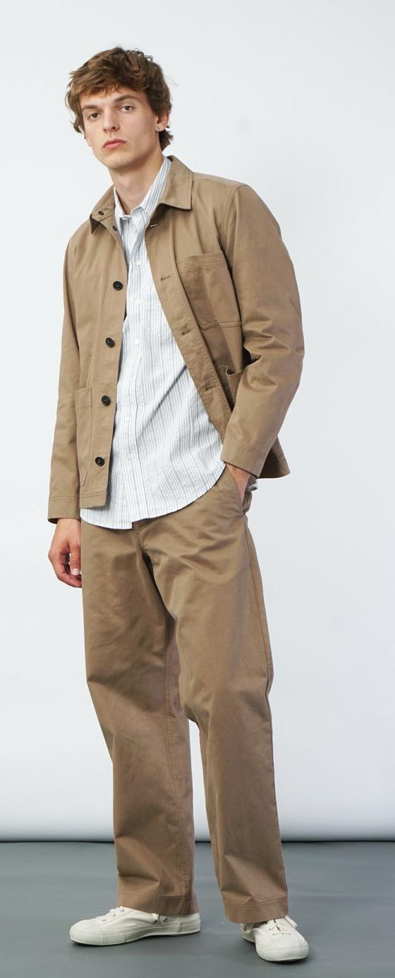 A man wearing a tan Hansen Garments chore jacket over a striped shirt with wide beige trousers