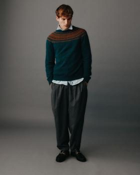 A man wearing a teal Fair Isle yoke sweater by Harley of Scotland with a blue shirt and grey pleated trousers