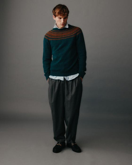 A man wearing a teal Fair Isle yoke sweater by Harley of Scotland with a blue shirt and grey pleated trousers
