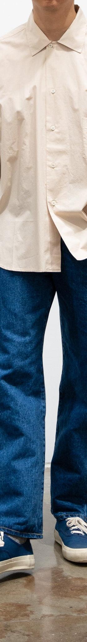 A man wearing wide-leg HATSKI selvedge jeans with an ecru short-sleeve shirt and navy sneakers
