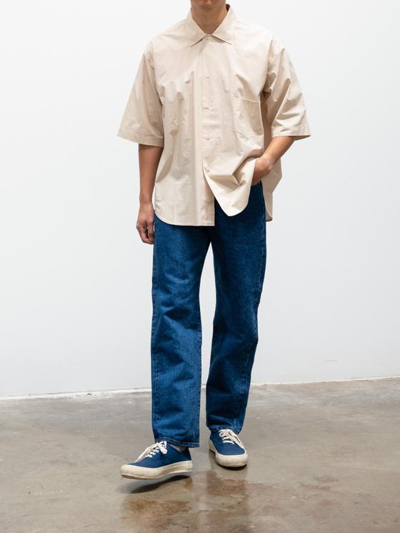 A man wearing wide-leg HATSKI selvedge jeans with an ecru short-sleeve shirt and navy sneakers