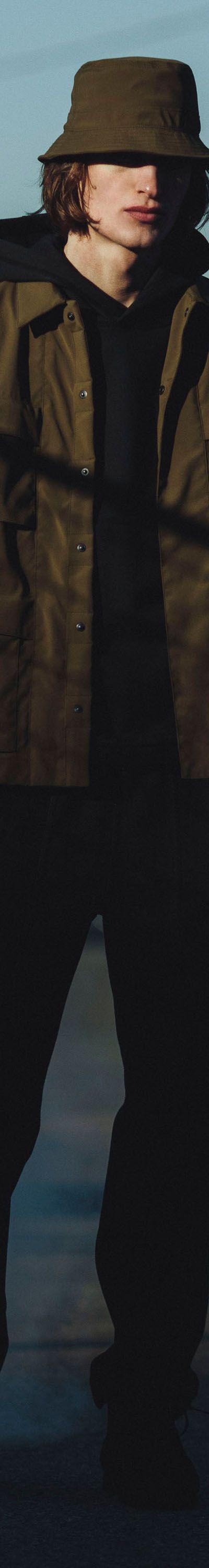 A man wearing an olive Haven field jacket, bucket hat and black trousers on a city street