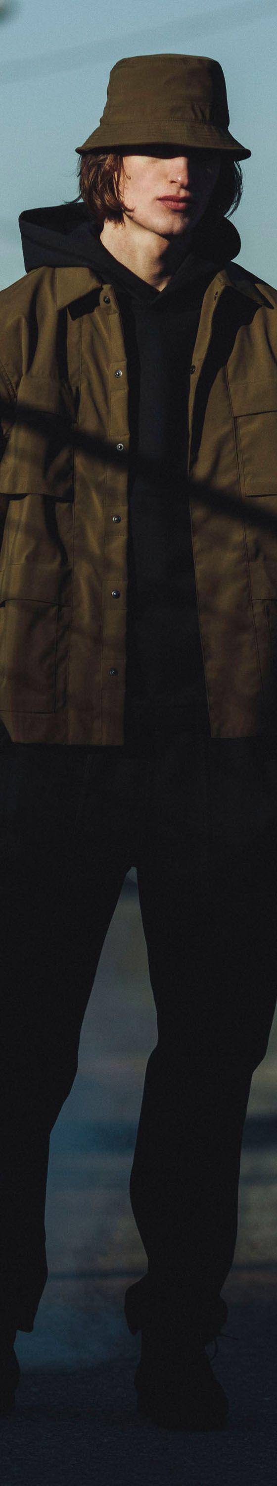 A man wearing an olive Haven field jacket, bucket hat and black trousers on a city street