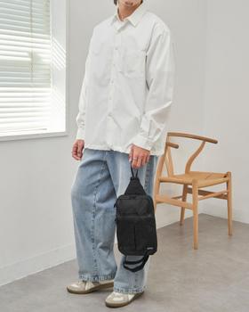 A man wearing a white oversized shirt and light-wash wide-leg jeans with a black sling bag