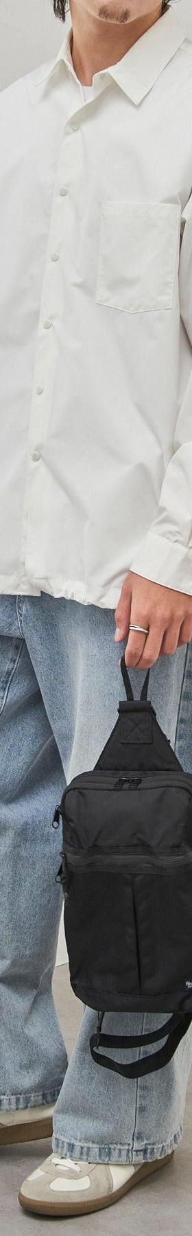 A man wearing a white oversized shirt and light-wash wide-leg jeans with a black sling bag