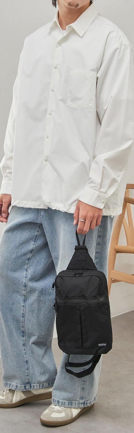 A man wearing a white oversized shirt and light-wash wide-leg jeans with a black sling bag