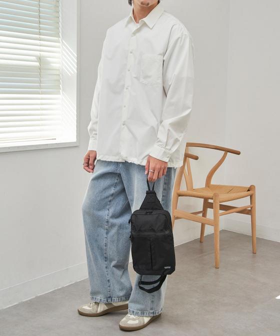A man wearing a white oversized shirt and light-wash wide-leg jeans with a black sling bag