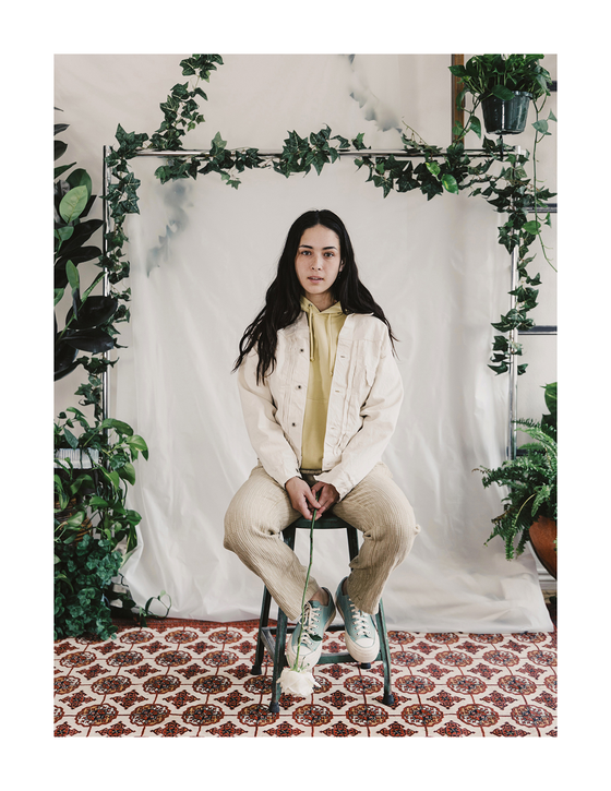A woman seated wearing a cream corduroy jacket, olive shirt and natural leather sneakers