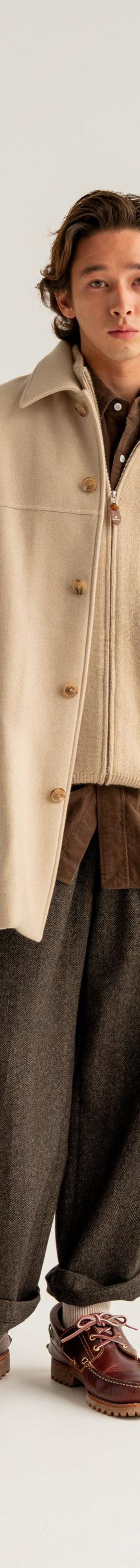 A man wearing a cream HERILL wool overcoat with brown flannel trousers