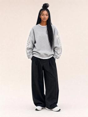 A woman wearing a grey hey hey studios sweatshirt with sleeve artwork and black wide-leg trousers