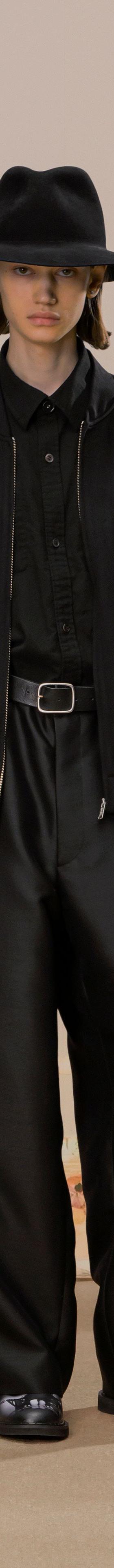 A model wearing a black bomber jacket with wide black trousers and a wide-brim hat