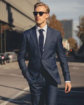 A man wearing a navy Hockerty suit with a white shirt and dark polka-dot tie