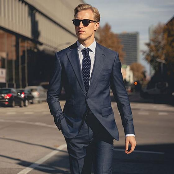 A man wearing a navy Hockerty suit with a white shirt and dark polka-dot tie