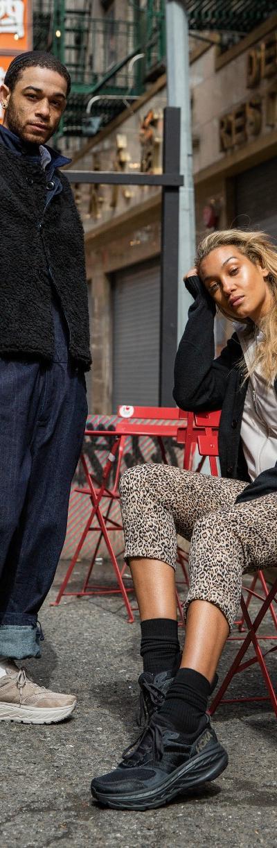 Two people wearing HOKA sneakers with layered streetwear on a city sidewalk