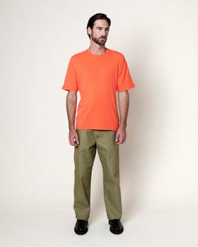 A man wearing an orange Homecore t-shirt with olive green trousers