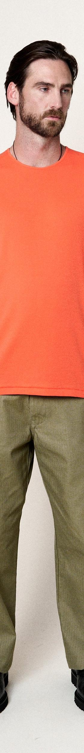 A man wearing an orange Homecore t-shirt with olive green trousers