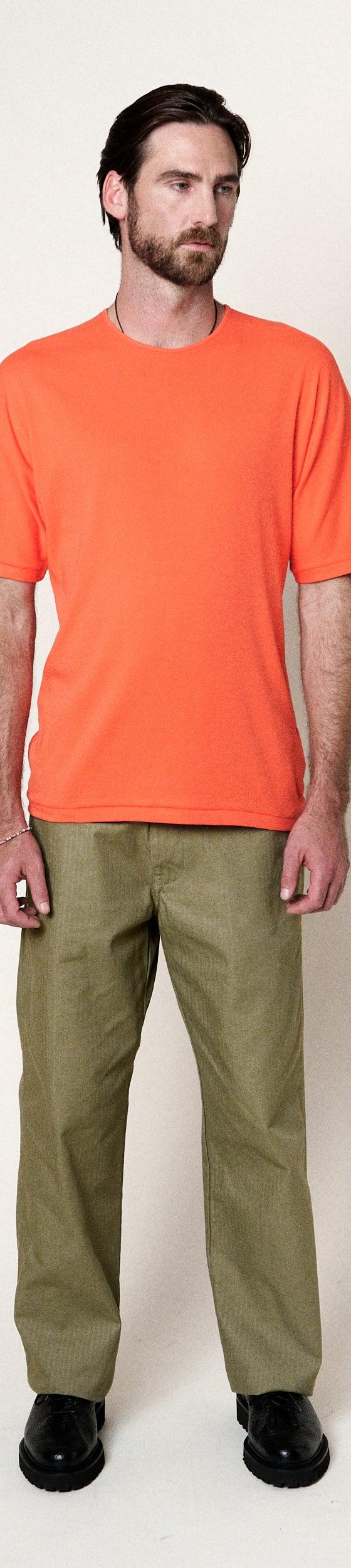 A man wearing an orange Homecore t-shirt with olive green trousers