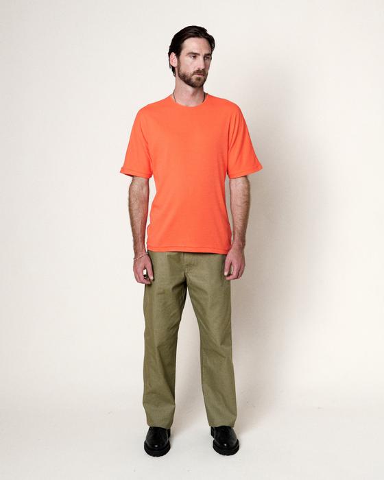 A man wearing an orange Homecore t-shirt with olive green trousers