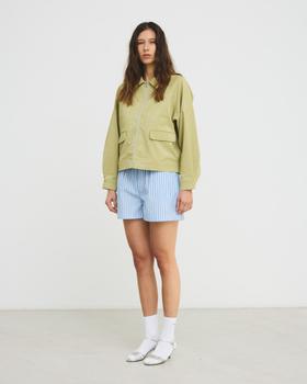 A woman wearing a pistachio green Hosbjerg jacket with blue striped shorts and white sandals