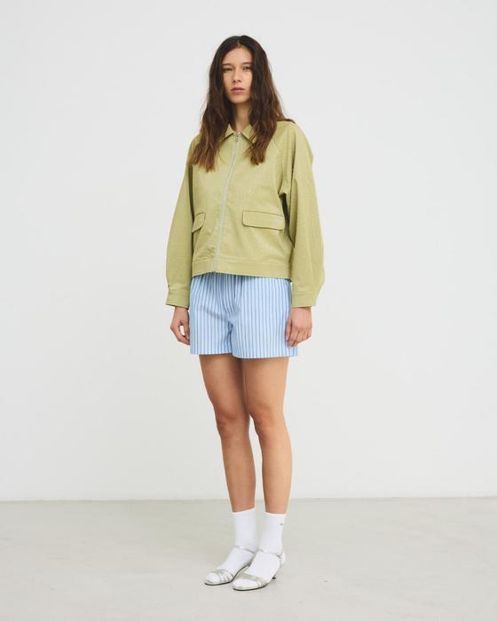 A woman wearing a pistachio green Hosbjerg jacket with blue striped shorts and white sandals