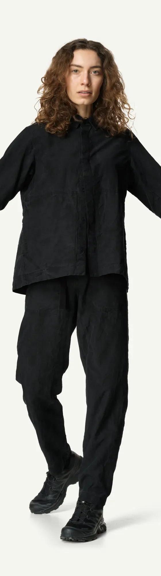 A woman wearing a black Houdini Sportswear overshirt and matching trousers