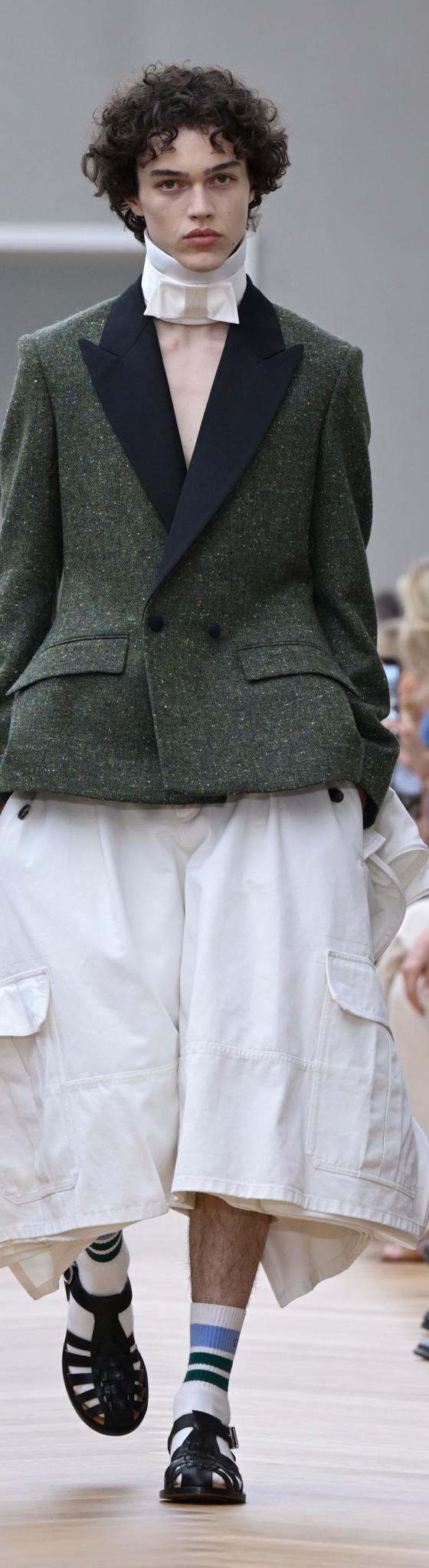 A man wearing a green tweed tuxedo-lapel jacket with wide white culottes